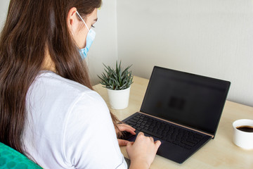 Young woman in medical mask working for laptop, portable computer from home on light background. Distance learning and work online, Corona virus (COVID19) protection