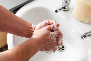 Man's hand wash his hands over sink in bathroom.