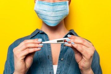 selective focus of young woman in medical mask holding thermometer on yellow background