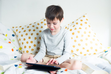 School Boy on bed at home with digital tablet in hand, doing homework. Distance learning online education. Quarantine