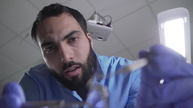 Patient point of view of handsome Middle Eastern dentist manipulating. Portrait of serious confident male stomatologist working in dental clinic. Medicine, dentistry, close-up.
