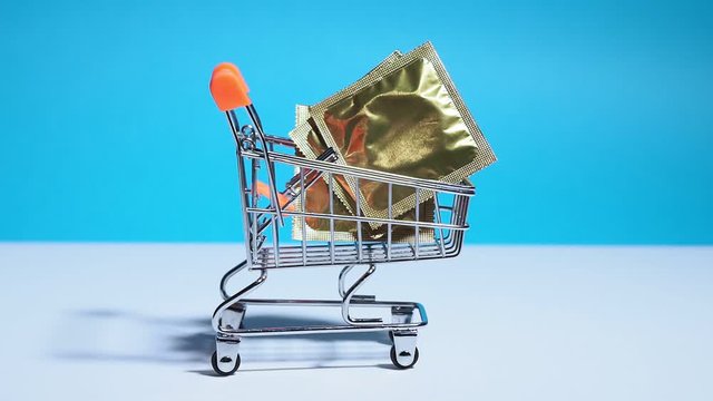 mini shopping cart with condoms on a colored background. purchase condom, concept, contraception