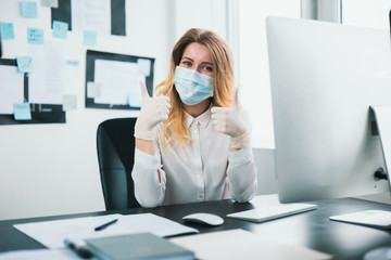 young blond woman manager in medical protection mask and gloves works in office during Covid-19...