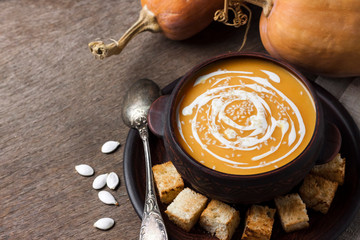 Pumpkin soup with cream and sesame seeds with croutons on wooden background