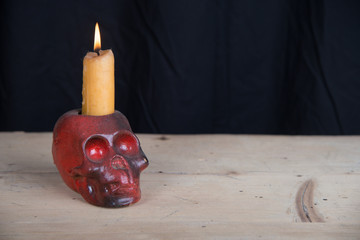 The concept of dark religion. Stone skeleton head with candle in it on wooden table