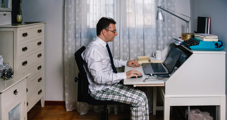 Man working from home with laptop wearing shirt, tie and pajama pants