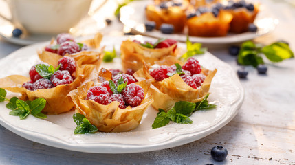 Phyllo cups with Mascarpone cheese filling topped with fresh raspberries and mint on a white plate. Delicious filo pastry dessert