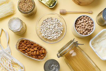 Creative flatlay with pantry staples. Glass jars with pasta, beans and chickpeas, canned goods, nuts and dried mushrooms in reusable containers. 