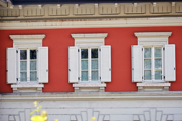Three Italian windows on the bright red color wall facade with opened wooden white shutters