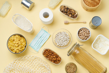 Top view of food staples prepared to survive Coronavirus COVID 19 pandemic at the time of cuarentine and home isolation. Pasta, chickpeas, nuts, cans and toilet paper. Flatlay on yellow background