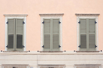 Italian window on the bright pink color wall facade with closed wooden khaki-green paint shutters