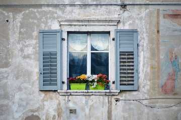 Fototapeta na wymiar Italian window on the old wall facade with open wooden shabby grey-blue paint shutters