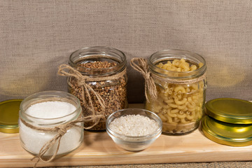 On the board are three open jars of pasta, buckwheat and sugar. Nearby are the covers and a bowl of rice.