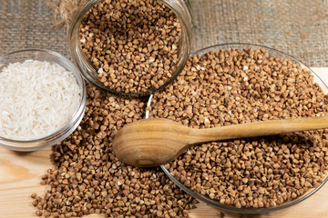 On the board lies buckwheat scattered, on a plate and in an inverted jar. A wooden spoon lies on top. A bowl of rice stands next to it.