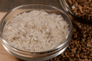 Close-up. Bowl with rice. Nearby are scattered grains of buckwheat.