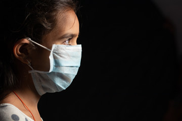 Young teenager girl with medical face mask in dark room at home quarantine due to covid 19 or...