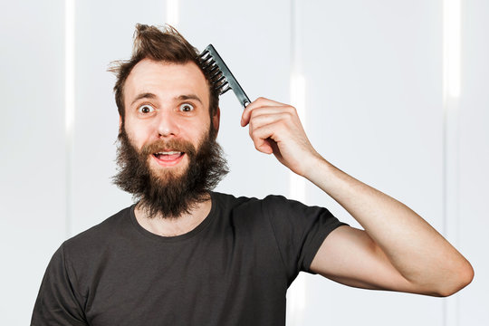 Young bearded overgrown man holding comb and combing his hair. For barbershop.