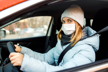 Woman in medical mask sitting at wheel in car during day.
