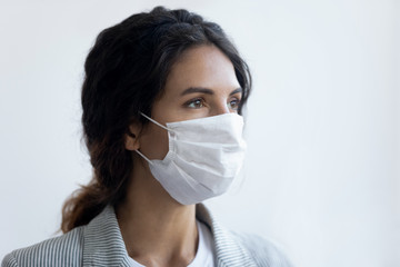 Hopeful young woman wear medical face mask protecting from coronavirus look in distance think of...