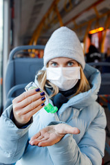 Fototapeta na wymiar Woman in medical mask looking at camera disinfects her hands with tool while sitting on bus