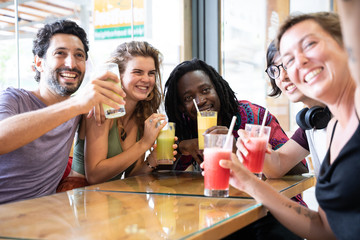 Group of people from different ethnicities making a selfie with a mobile phone sitting and drinking fruit juices