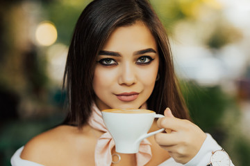 Close-up portrait of attractive young woman drinking coffee at cafe. Pretty woman enjoying her morning coffee on a terrace in the city.