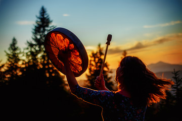 beautiful shamanic girl playing on shaman frame drum in the nature.