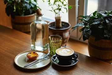 cup of coffee with foam and cake on a plate with cutlery