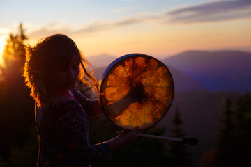 beautiful shamanic girl playing on shaman frame drum in the nature.