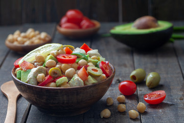 Homemade salad with avocado, chickpeas, mixed vegetables and chicken in rustic wooden bowl. Healthy dietary food.
