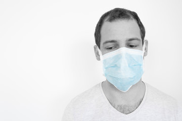 Closeup of a young man wearing a biomedical mask in tears during the pandemic crisis, black and white with blue color on the mask
