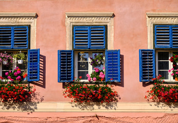 Fototapeta na wymiar Upper floor window with blue shutters and flower pots and hanging baskets.