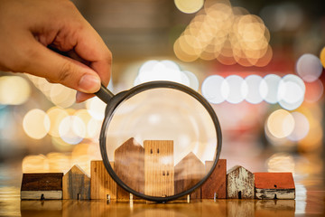 Hand holding magnifying glass and looking at house model, house selection, real estate concept.