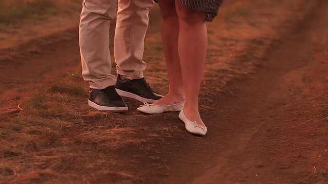 Close-up of a couple in love walking along a country road in the summer at sunset, slow motion.