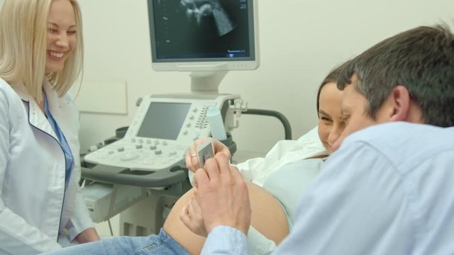 A woman doctor gives photos of an ultrasound scan to a pregnant woman. The girl was expecting a newborn baby. Happy couple watching a picture and smiling