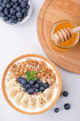 Breakfast with yogurt, granola, mint, bananas, honey and blueberry on white concrete background. Flat lay composition
