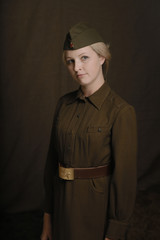 Portrait young blonde woman in military uniform from second world war stands and looks at lens of...