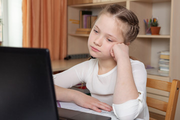 Sad schoolgirl looks at a laptop screen. Distance learning online education, home school, home education, quarantine concept