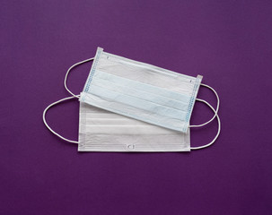 two disposable medical masks on purple background.