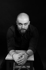 mysterious black and white portrait of a man with a beard in a black coat on a black background in a photo studio