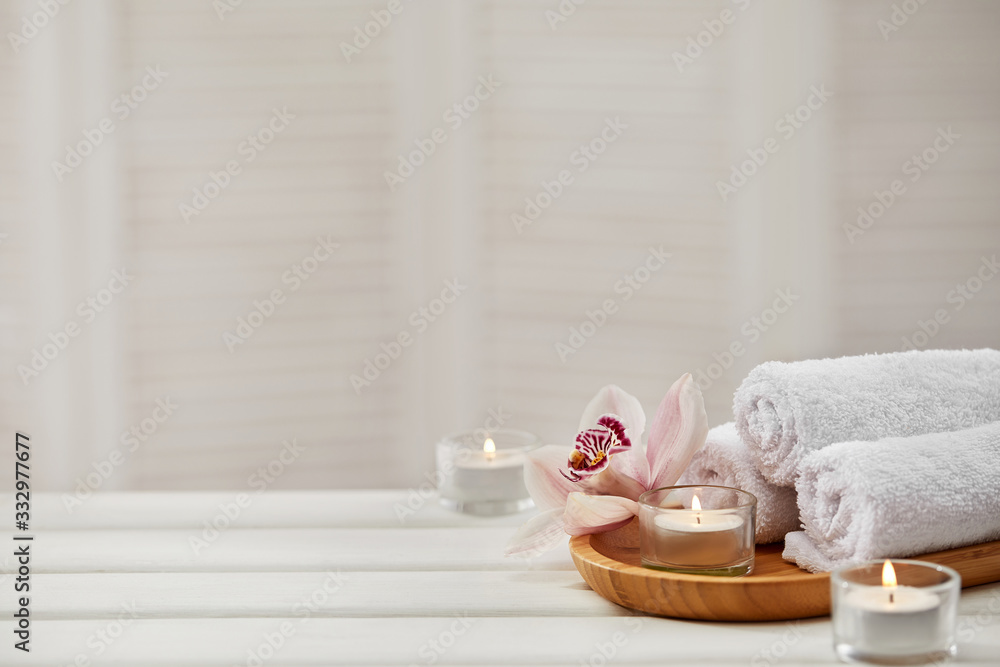 Wall mural Spa composition with aromatic candles, orchid flower and towel on white wooden table. Beauty spa treatment. copy space