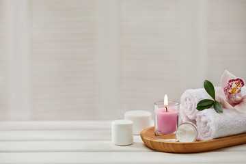 Spa products with aromatic candles, orchid flower and towel on white wooden table. Beauty spa...