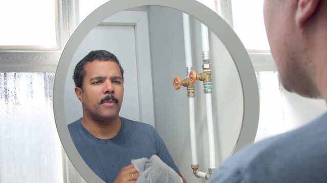man behind the mirror during his morning facial care routine dru his face with towel and put some facial cream aftershave