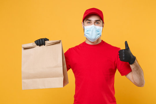 Delivery man employee in red cap blank t-shirt uniform mask glove hold craft paper packet with food isolated on yellow background studio Service quarantine pandemic coronavirus virus 2019-ncov concept
