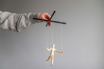 The human hand holds a wooden doll on the clothesline on a gray background with place for text....