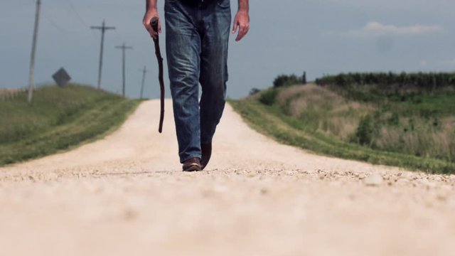 Man with cowboy boots and blue jeans walks on road to camera slow motion