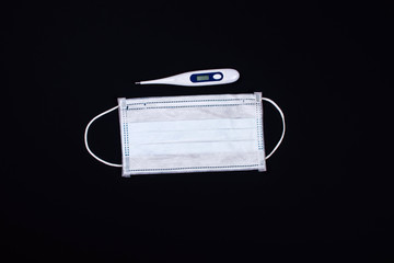Thermometer and medical face mask on contrast black background