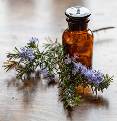 Rosemary essential oil and fresh blooming twig on a wooden table,