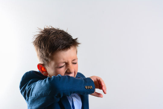 Unhappy Kid Cough Into His Elbow, Not His Hand. Small Boy Pull The Collar Of Her T-shirt Up To Cover Mouth When Coughing. Coughing Advice From Experts Who Seek To Minimize Risk Of Viral Transmission