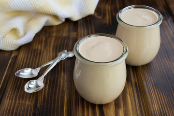 Homemade ryazhenka in the glass jars on the brown wooden  background. Fermented milk product....